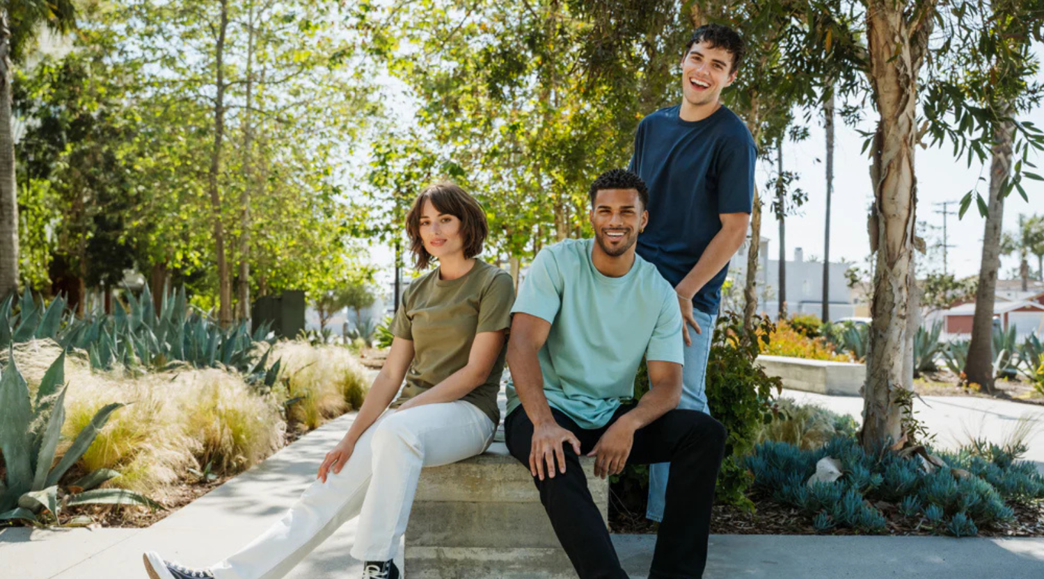 Three people sitting on a bench with trees behind them with a girl in a green t-shirt and two boys in blue.